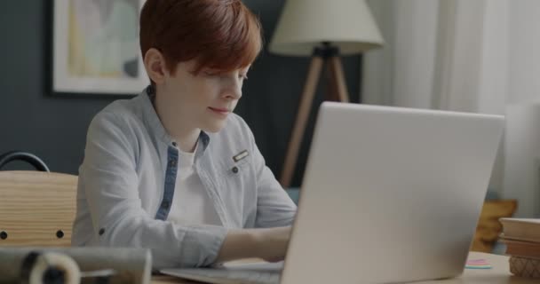 与笔记本电脑一起工作的多愁善感的男孩在家里的办公桌前享受在线教育 青少年打字主要是为了从互联网上获取信息 — 图库视频影像
