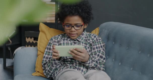 一个快乐的非洲裔美国孩子在家里玩网络游戏 带着智能手机微笑在沙发上放松的肖像 现代设备和娱乐概念 — 图库视频影像