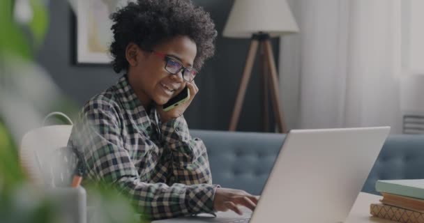 ラップトップのタイピングや自宅で携帯電話で話してかわいいアフリカ系アメリカ人の少年 コミュニケーションと現代技術の概念 — ストック動画