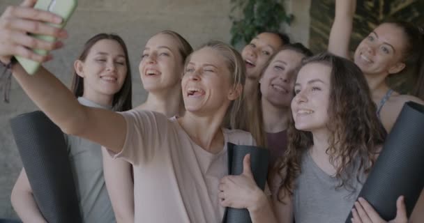 現代のスタジオでヨガマットで自撮りをするスマートフォンカメラのポーズをとる若い女性のグループ 写真と現代技術の概念 — ストック動画
