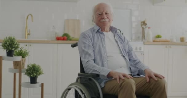 老人は台所の車椅子に座り 老人ホームでカメラを見ている 老人と家庭生活の概念 — ストック動画