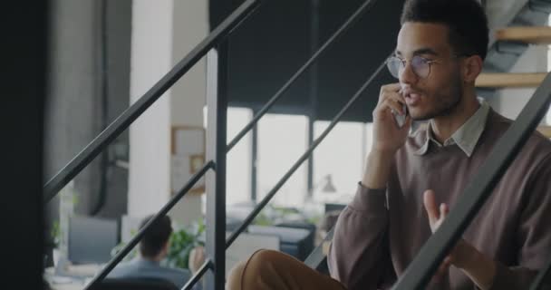 员工非裔美国人坐在同事中心的楼梯上 用手机与客户交谈 为客户提供支持 公司和商业交流概念 — 图库视频影像