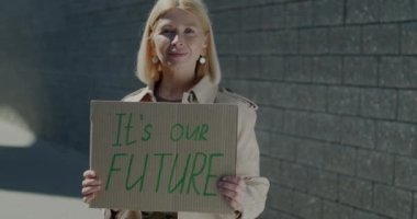 Olgun bir kadın aktivistin elinde tutması geleceğe dair işaretimiz ve arkamızdaki tuğladan duvara yaslanmış gülümsememiz. İnsanlar ve farkındalık kavramı.