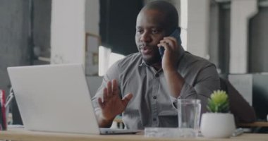 Cep telefonuyla konuşan ve ofiste laptop kullanan hırslı bir Afrikalı Amerikalı. İş iletişimi ve teknoloji kavramı.