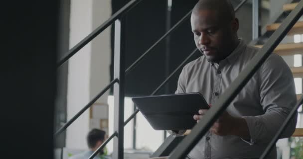 非裔美国商人坐在办公室楼梯上 用平板触摸屏 商务概念用现代技术和便携式设备 — 图库视频影像