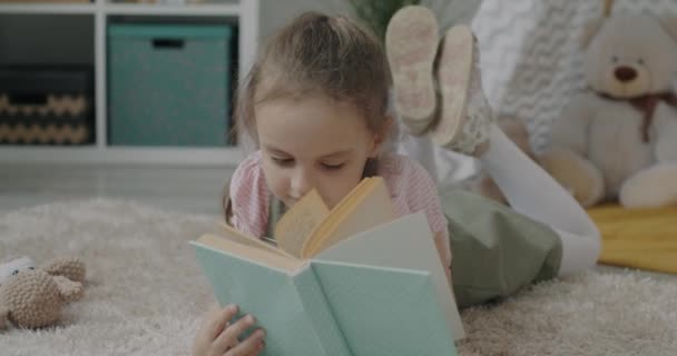Jolie Petite Fille Lecture Livre Couché Sur Sol Maison Souriant — Video