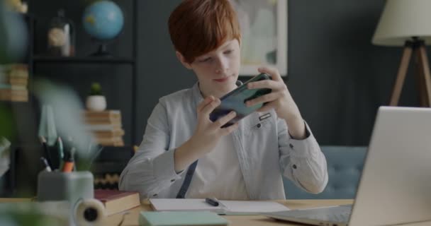 アパートで面白いスマートフォンの画面に触れるオンラインビデオゲームをプレイ楽しい十代の男の子 現代のテクノロジーとゲームのコンセプト — ストック動画