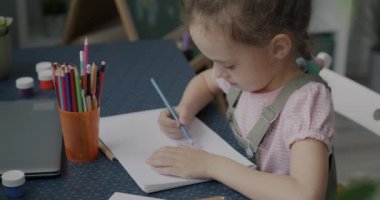 Yaratıcı küçük kız kalemlerle resim çiziyor. Evde masada otururken ilham geliyor. Mutlu çocukluk ve sanat konsepti.