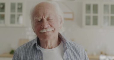Mutfakta mutlu bir yüzle kameraya bakan gülümseyen emekli adamın portresi. Olumlu duygular ve neşeli yaşlı insanlar konsepti.
