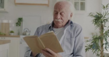 Mutlu emekli adam kitap okuyor. Modern mutfakta tek başına oturup ilginç hikâyeler anlatıyor. Edebiyat ve mutlu emeklilik kavramı.