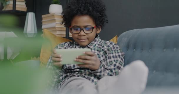 快乐的非裔美国男孩玩电子游戏 带着智能手机笑着在家里享受活动 童年和现代技术概念 — 图库视频影像