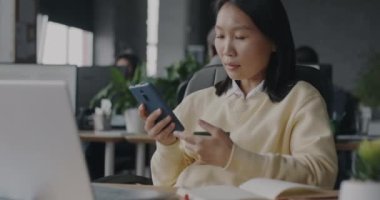 Güzel Asyalı kadın akıllı telefon ve kredi kartıyla iş yerinde para transferi yapıyor. İş ve finans teknolojisi kavramı.