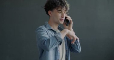 Neşeli adam cep telefonuyla konuşuyor gri arka planda el kol hareketi yapıyor ve gülümsüyor. Mobil iletişim ve modern yaşam tarzı kavramı.