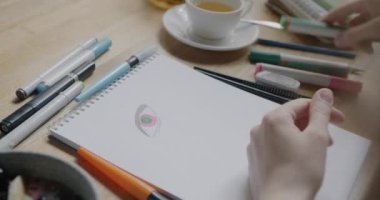 Kafedeki masada sanattan zevk alan kalemlerle kağıda göz resmi çizen tasarımcının yakın çekimi. Profesyonel meslek ve yaratıcı aktivite kavramı.