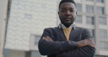 İyi giyimli, şık takım elbiseli bir Afro-Amerikan 'ın şehirde dikilip ciddi bir yüzle kameraya bakışının yavaş çekim portresi. Halk ve şehir yaşam tarzı kavramı.