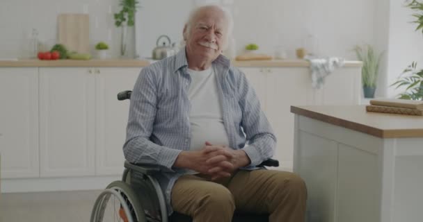 自宅のモダンなキッチンルームでカメラを見て車椅子に座って穏やかな老人 障害者の移動と退職の概念 — ストック動画