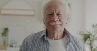 Sağlıklı yaşlı bir adamın portresi. Evdeki mutfakta neşeli bir gülümsemeyle kameraya bakıyor. Emeklilik ve yaşlılık kavramı.