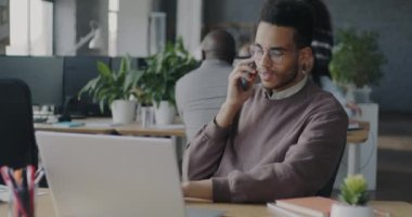 Ofis çalışanı Afro-Amerikan adam cep telefonuyla iş görüşmeleri yapıyor ve dizüstü bilgisayar kullanıyor. İş iletişimi ve meslek kavramı.