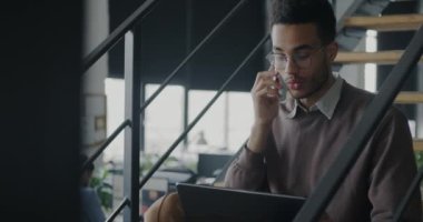 Afrika kökenli Amerikalı iş adamının portresi cep telefonuyla konuşuyor merdivenlerde oturmuş projeyi tartışıyorlar. İletişim ve iş konsepti.