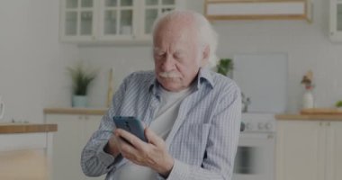 Mutlu son sınıf öğrencisi akıllı telefon mesajları atıyor ve gülümsüyor. Mutfaktaki modern teknolojinin tadını çıkarıyor. Emeklilik ve iletişim kavramı.