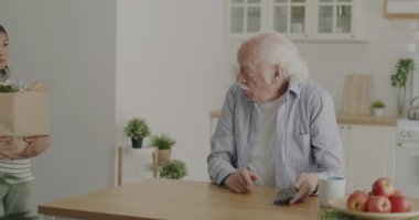 Sevgi dolu genç bir kadın markete yiyecek getiriyor. Mutfaktaki büyük babaya yemek veriyor. Yemek teslimatı ve aile ilişkileri konsepti.