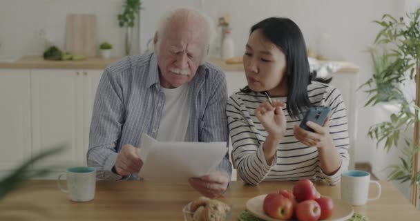 Nurse Asian Woman Helping Senior Caucasian Man Taxes Counting Smartphone — Stock Video