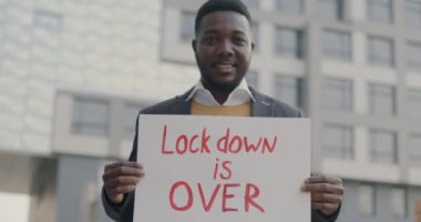 Kilitlenen mutlu Afro-Amerikalı adamın yavaş çekimde çekilmiş portresi açık havada kameraya bakıp gülümsüyor. İnsanlar ve salgın konsepti.