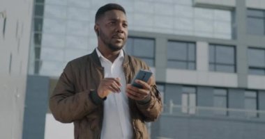 Şehir caddesinde duran kablosuz kulaklıkla konuşan Afro-Amerikan bir adamın portresi. Modern teknoloji ve iletişim konsepti.