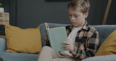 Düşünceli çocuk evde kanepede oturmuş kitap okuyor boş zamanlarında yalnız başına dinleniyor. Modern edebiyat ve yerli eğitim kavramı.