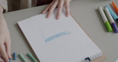 Çizim defterine yakın çekim ve kadın pastel boyalarla resim çizerken bir yandan da masa başında yaratıcı hobilerin keyfini çıkarıyor. Sanat ve kültür konsepti.