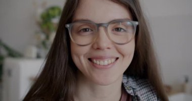 Evdeki mutfakta gülümseyen ve gözlüklere dokunan mutlu genç bir kadının yakın plan portresi. Gençlik ve şık gözlük konsepti.