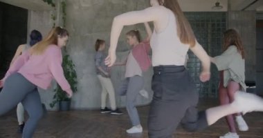 Modern kıyafet giymiş, yaratıcı stüdyoda çağdaş dans eden mutlu genç kadınların ağır çekimleri. Modern hareketler öğrenen kız öğrenciler.