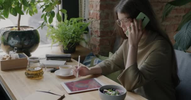 グラフィックタブレットで女性のデジタルアーティストの描画を作成し カフェで携帯電話でクライアントと話をします デバイスとフリーランスの仕事のコンセプト — ストック動画