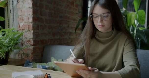 グラフィックタブレットやコーヒーを片手にカフェでリモートワークを楽しむ若い女性デザイナー 現代技術と遠い仕事の概念 — ストック動画