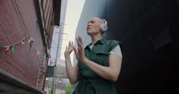 都会のパフォーマンスの間に屋外で踊るかなり若い女性の低角度ショットヘッドフォンを身に着けている レジャー活動と人々のコンセプト — ストック動画
