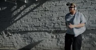 Kulaklık takan yaratıcı öğrencinin yavaş çekim portresi. Güneşli yaz gününde, dışarıda dinlenen müziğin keyfini çıkarıyor..