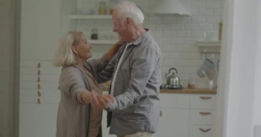 Mutlu yaşlı çift el ele dans ediyor evde dinleniyor ve mutfakta romantik müzik dinliyor. Aile hayatı ve eğlence konsepti.