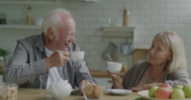 İki yaşlı adam ve kadın kahve fincanı içip mutfakta sohbet ediyorlar. Aile ilişkisi ve çay saati konsepti.