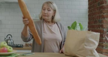 Yaşlı bir kadının portresi. Evdeki yiyecek paketlerini açıyor. Mutfaktan alışveriş yapıyor. Beslenme ve ev hayatı kavramı.