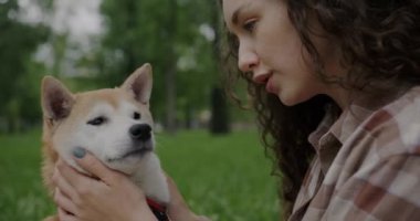 Yavaş çekimde, parkta Shiba Inu köpeğini öpen ve okşayan nazik genç bir kadının portresi. Hayvan ve doğa kavramı.