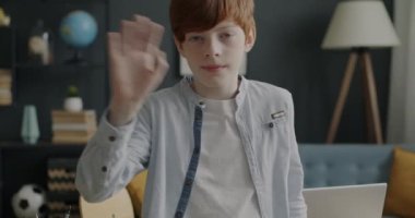 Evinde el sallayan ve gülümseyen bir gencin yavaş çekim portresi. Pozitif duygu ve merhaba işareti kavramı.