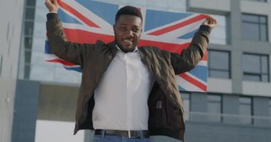 Büyük Britanya 'nın bayrağını sallayan Afro-Amerikan bir adamın yavaş çekim portresi. Açık havada gülümsüyor. Ülke ve milliyet kavramı.