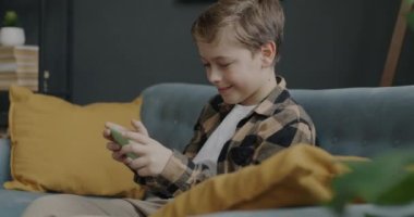 Heyecanlı çocuk video oyunu oynayarak eğleniyor. Evdeki kanepede oturup gülüyor. Oyun ve modern aletler konsepti.