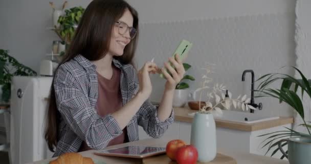 快乐的年轻女人坐在厨房的餐桌旁 用智能手机发短信 现代装置和互联网通信概念 — 图库视频影像