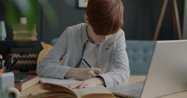 聪明的男孩在书本上读书 在笔记本上写信息 忙着在公寓的桌子边做作业 教育和儿童概念 — 图库视频影像