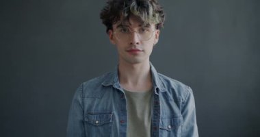 Yavaş hareket eden genç adam el hareketi yapıyor ve gri arka planda gülümsüyor. Pozitif geribildirim ve milenyum konsepti.