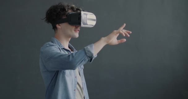 戴着虚拟现实眼镜的年轻人带着胳膊在灰色背景下享受着现代设备 人与技术概念 — 图库视频影像