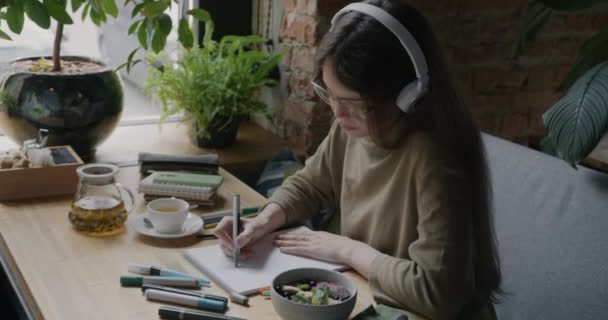 Glückliche Junge Designerin Zeichnet Café Skizzen Und Hört Musik Über — Stockvideo