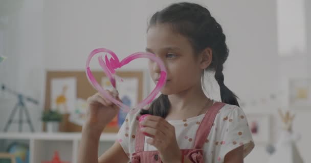 アパートの窓にピンクのハートを描く愛情のある子供のスローモーション 美しい女の子は芸術に集中した創造的な活動を楽しんで — ストック動画