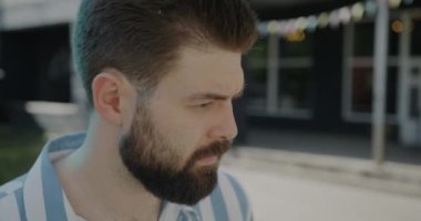 Düşünceli bir adamın portresi kameraya dönüyor ve açık havada şehrin arka planında gülümsüyor. Mutlu insanlar ve olumlu duygu kavramı.